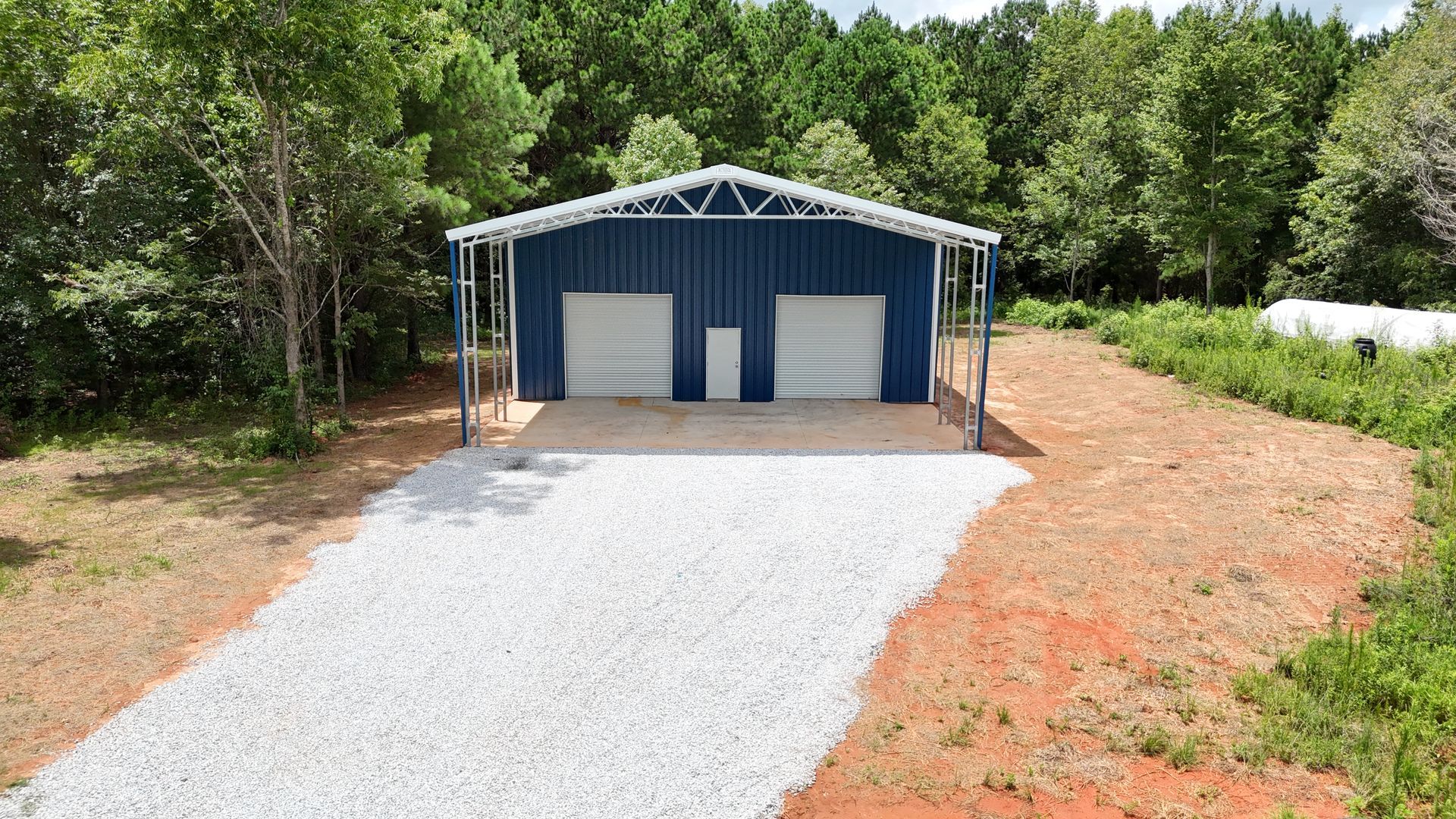 A blue garage with two garage doors is sitting on top of a gravel driveway.