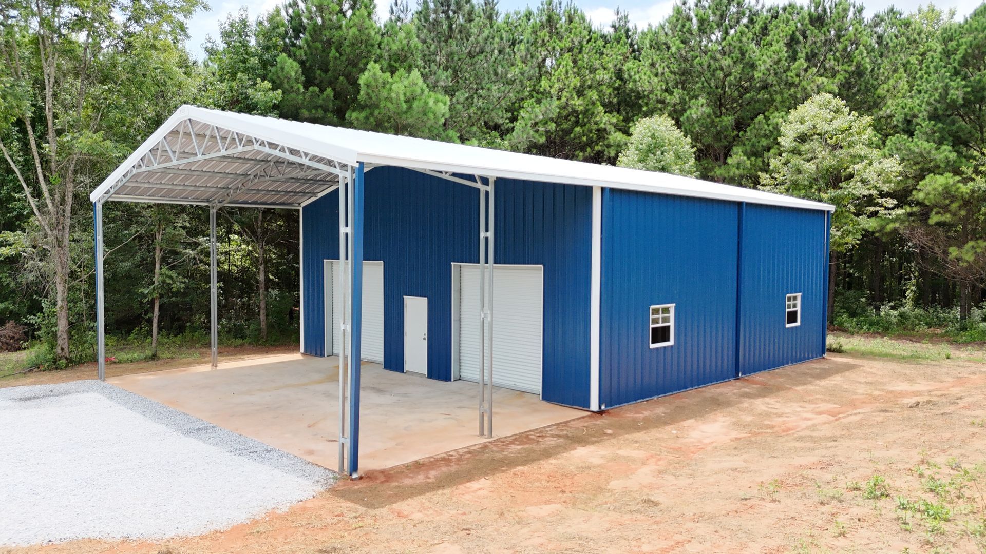 Blue metal shed with a carport in a wooded area.
