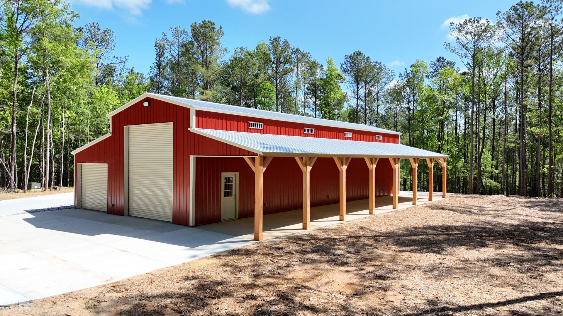 A large red barn with a covered porch in the middle of a forest