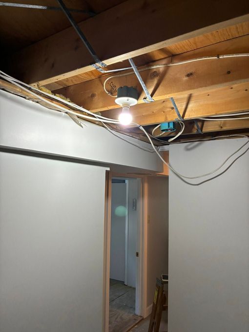 Exposed ceiling with wires and a light fixture. Room with a doorway and white walls.