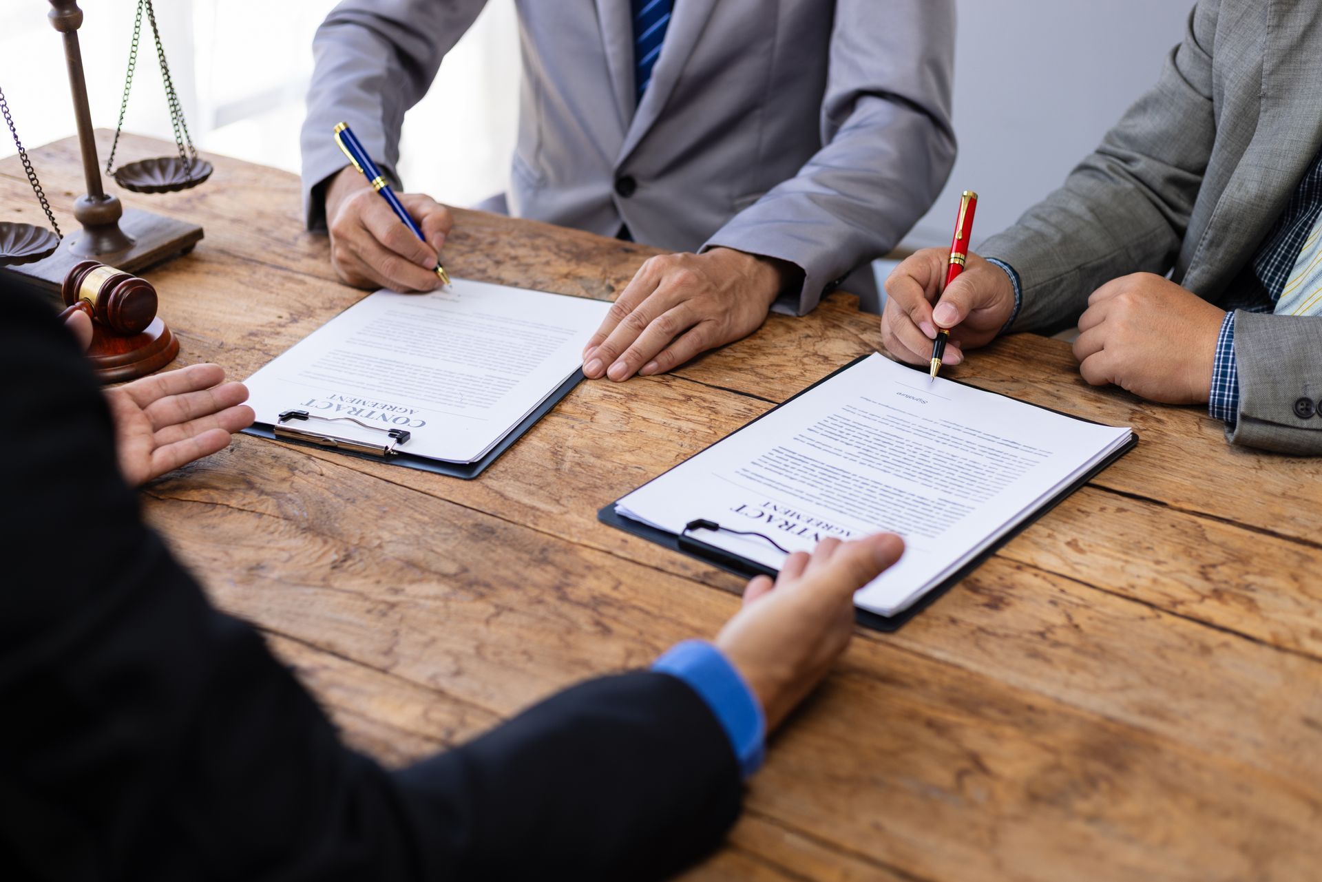 A lawyer is discussing a document with two clients in an office with a gavel and scales on a table.
