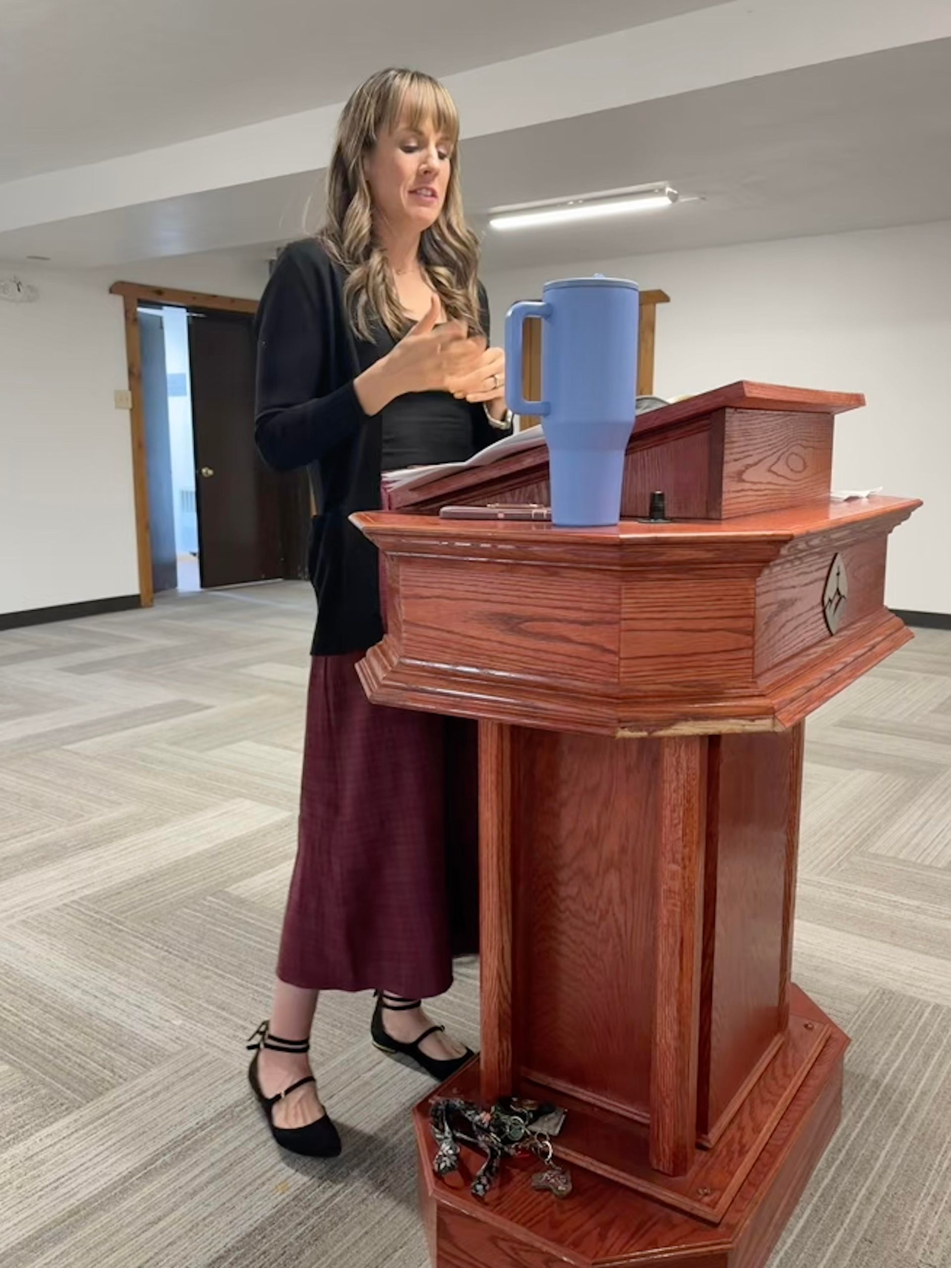 A woman is standing at a podium in a room with a christmas tree in the background.
