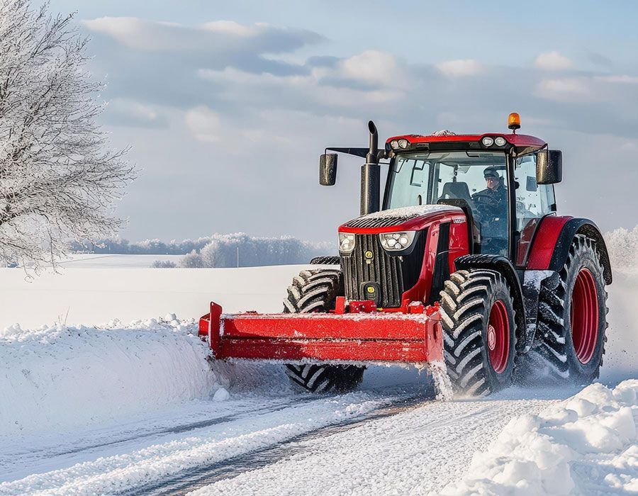 Red tractor plowing snow on a snowy road in a winter field