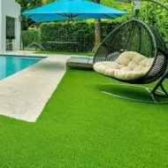 Poolside patio with green turf, blue umbrella, and hanging egg chair beside the water