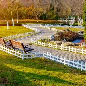 Winding park path with white fence, wooden bench, pond, and autumn trees in bright sunlight