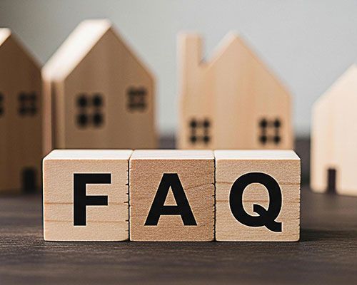 Wooden blocks spelling “FAQ” on a table, with blurred house models in the background.