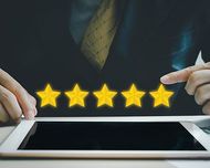 Hands holding a tablet with five glowing gold stars above it on a dark background