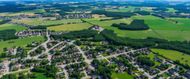 Aerial view of a small village with houses, roads, and surrounding green farmland under clear skies