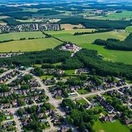 Aerial view of a small village with houses, roads, and surrounding green farmland under clear skies