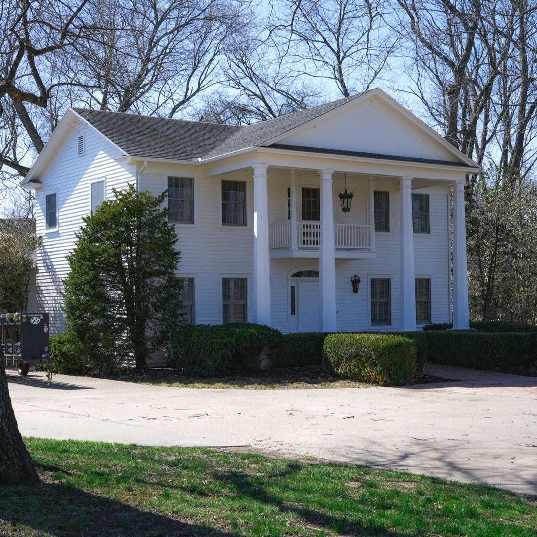 A large white house with a porch and trees in the background