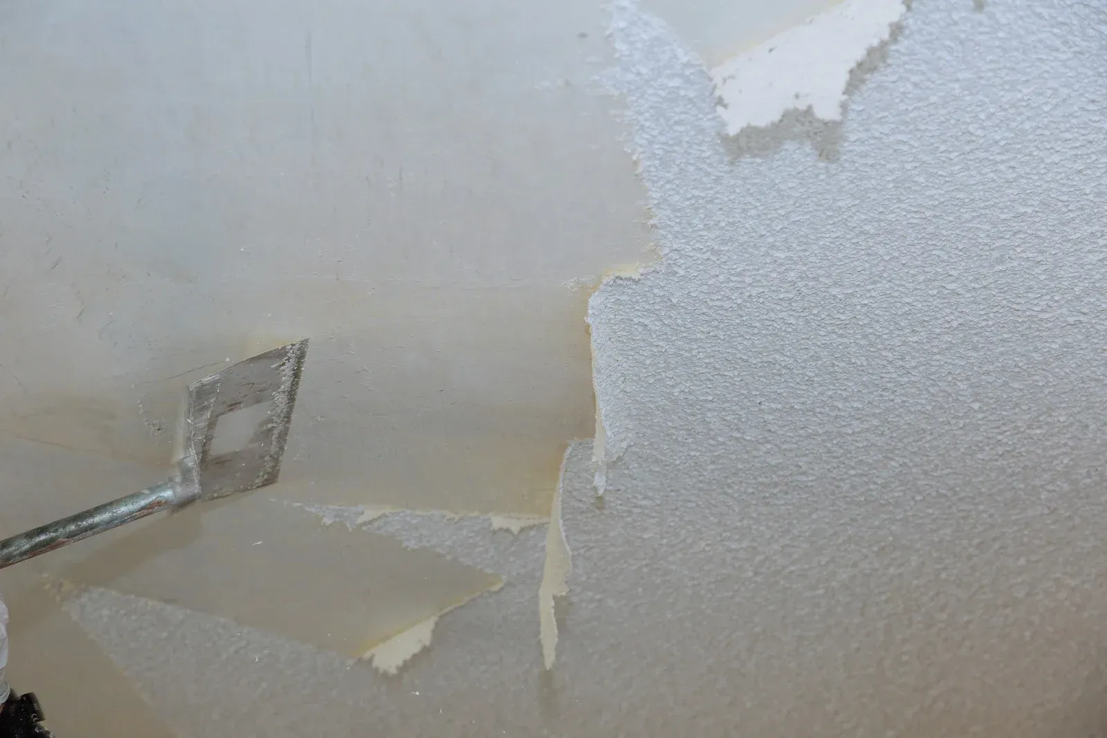 A person is removing wallpaper from a wall with a spatula.