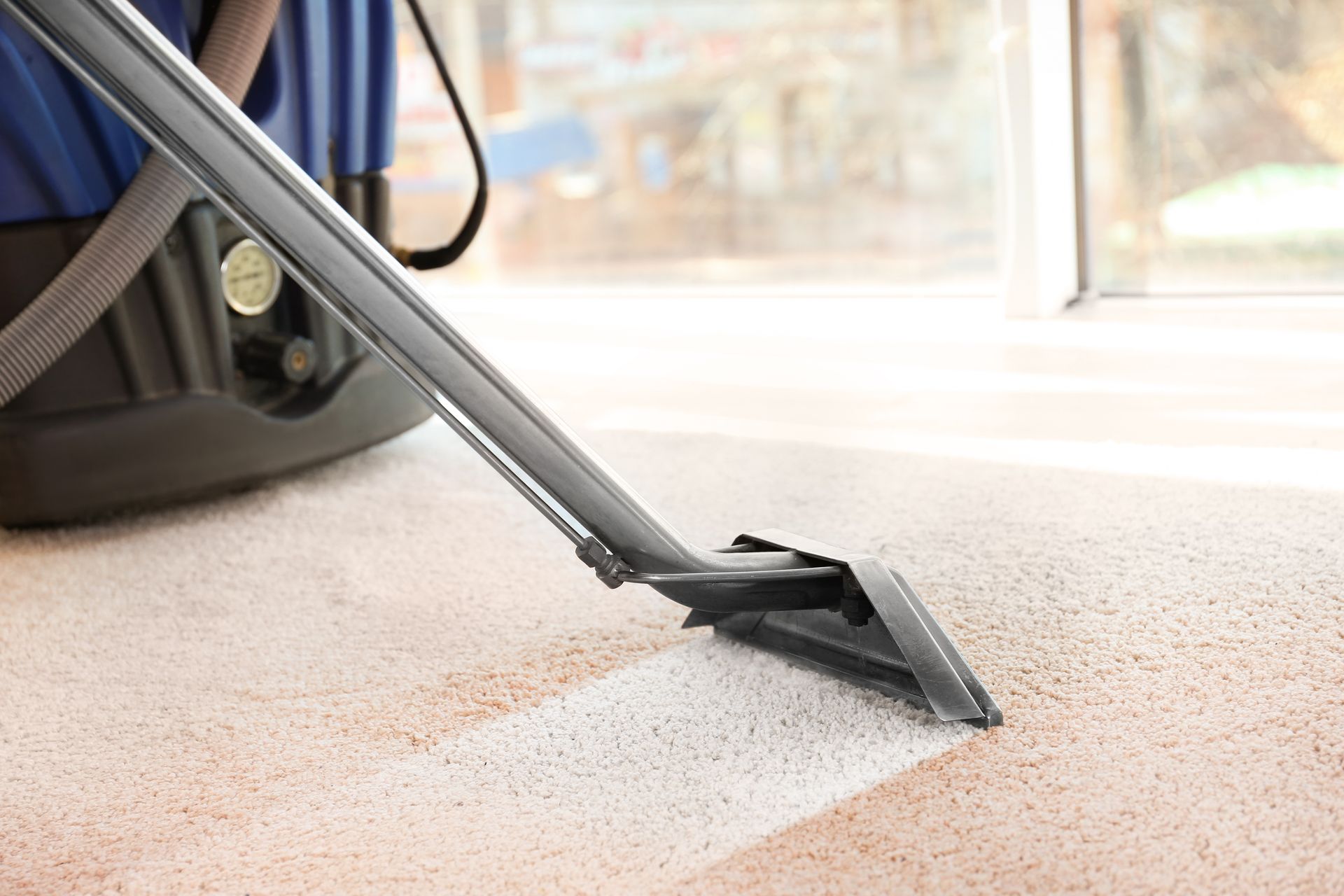 Vacuum nozzle cleaning dust from a carpet near a window
