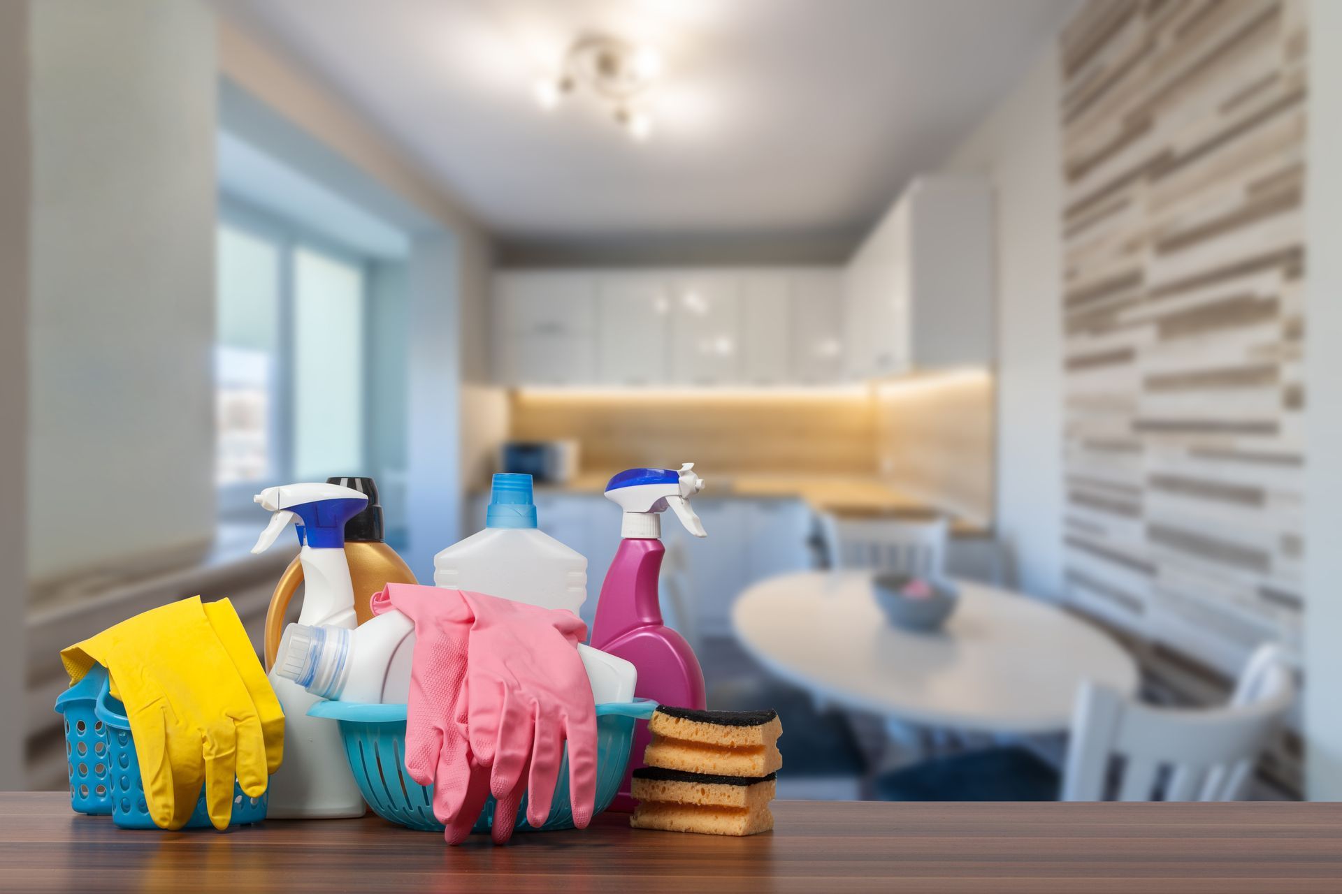 Cleaning supplies on a counter in a bright, modern kitchen with a blurred dining area behind.