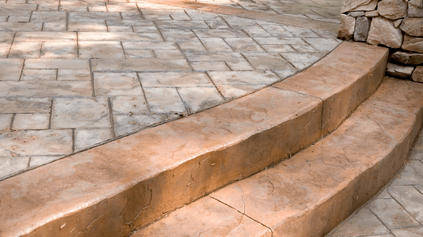 “Decorative stamped concrete patio with a raised step and textured stone-style surface from concrete services in Casas Adobes, AZ”