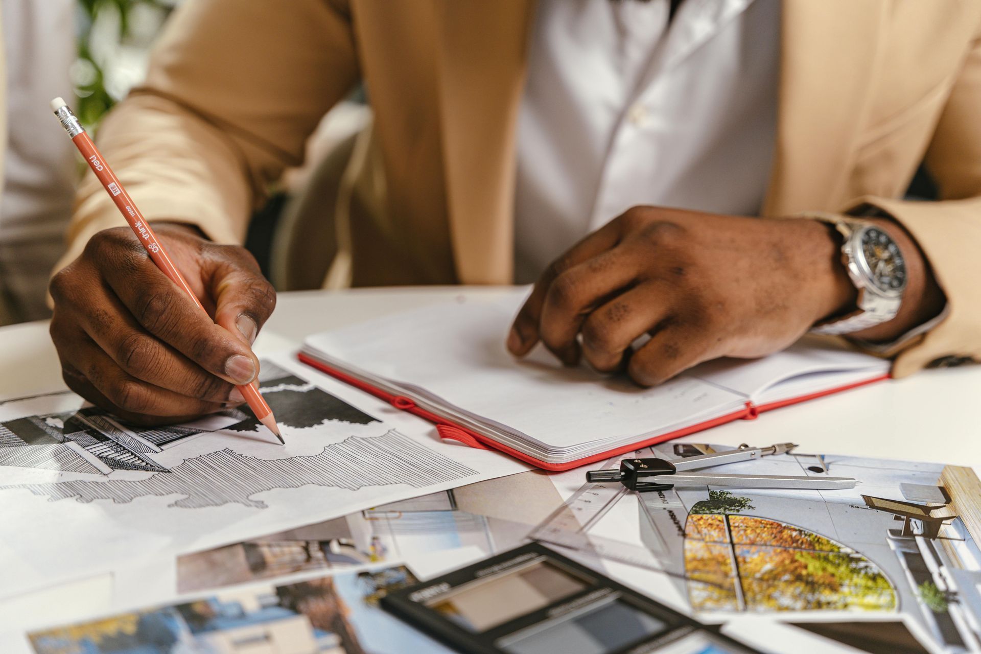 A man is sitting at a table drawing with a pencil in a notebook.