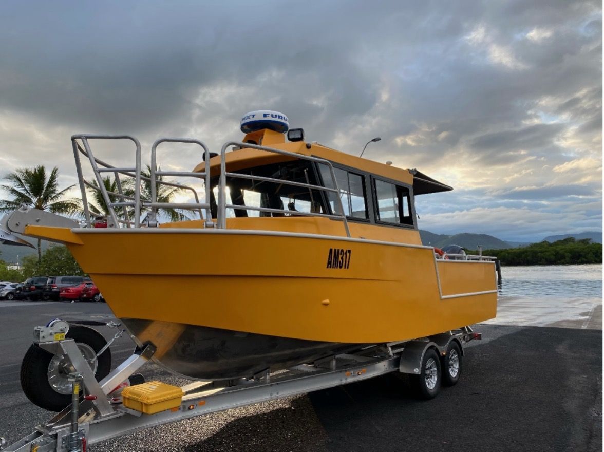A yellow boat is on a trailer next to a body of water.