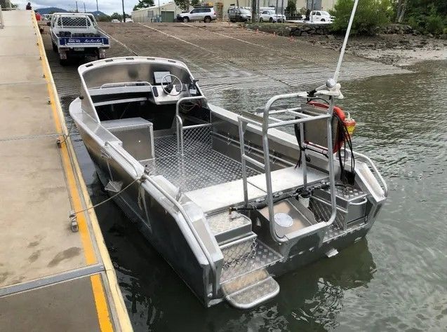 A silver boat is docked at a dock in the water.