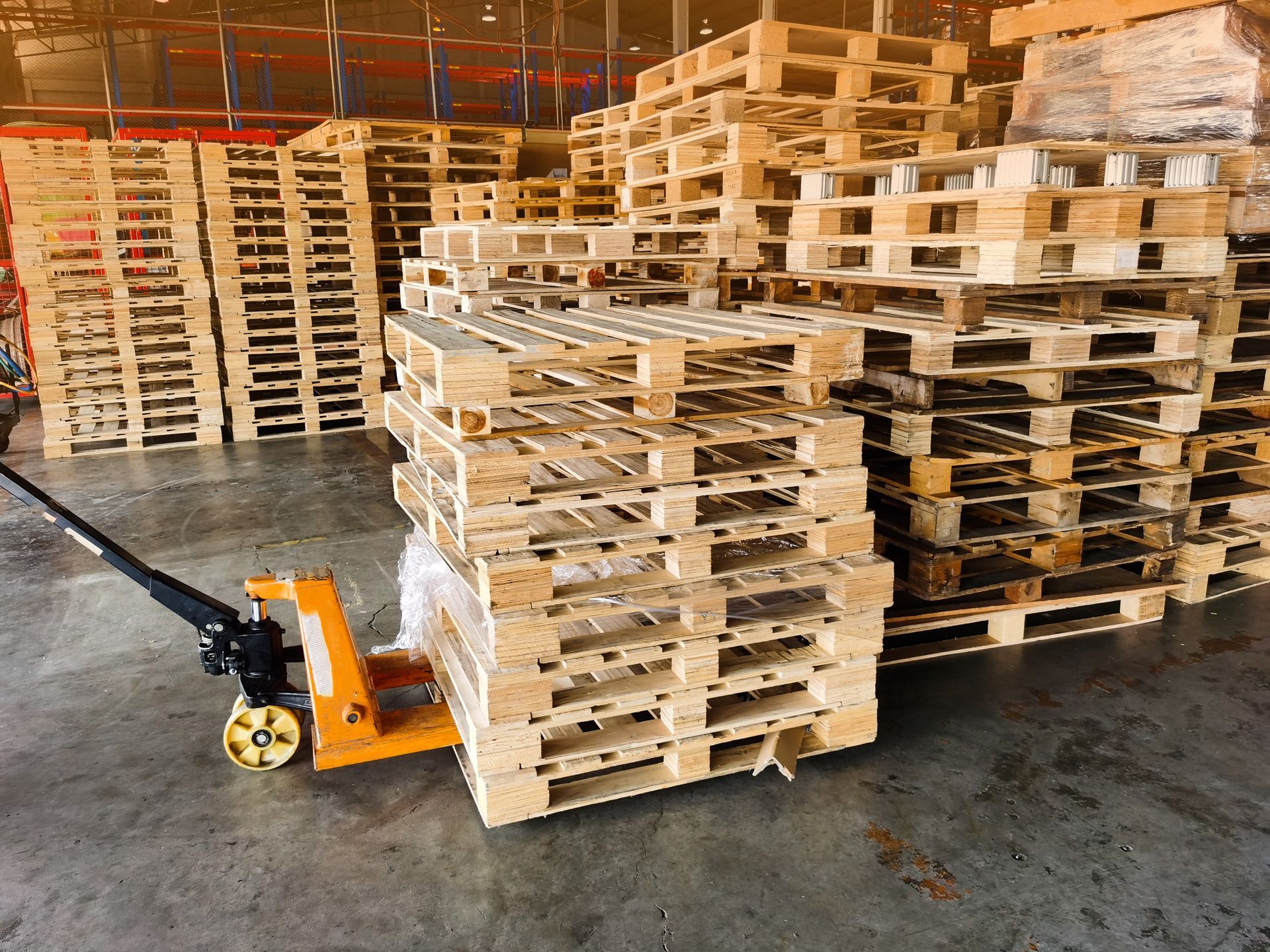 A pallet truck is pushing a pile of wooden pallets in a warehouse