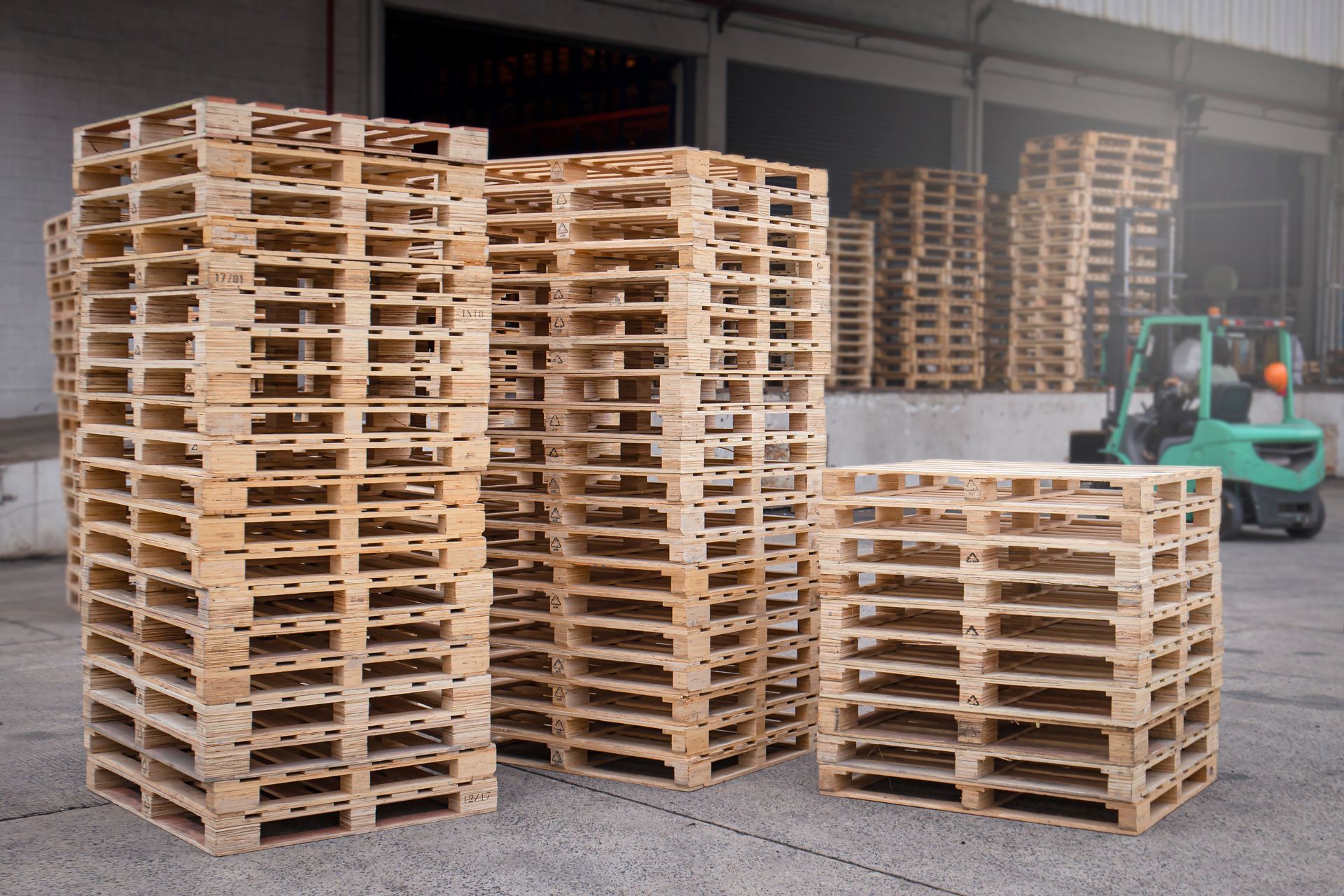 A stack of wooden pallets in a warehouse with a forklift in the background
