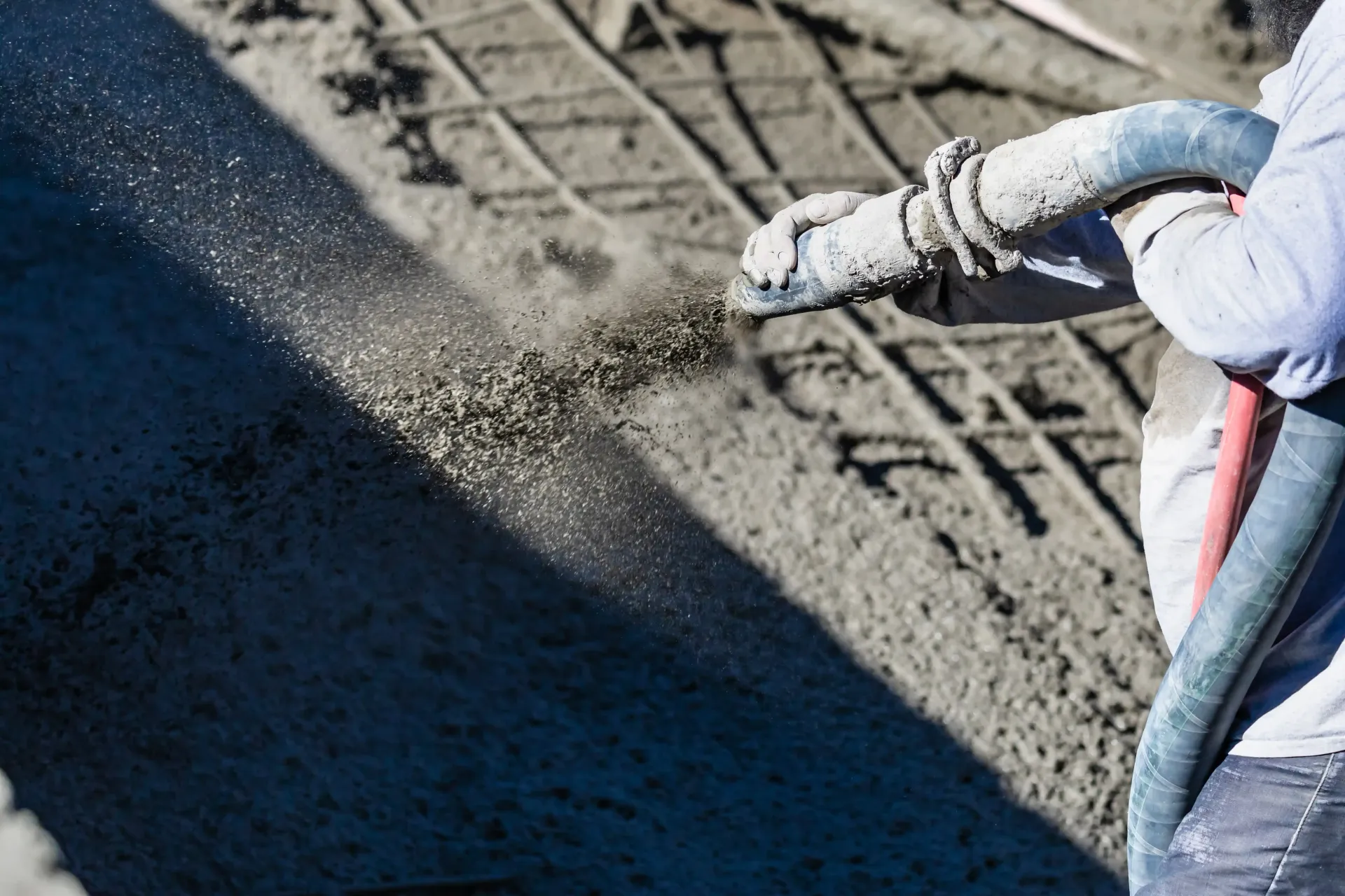Person spraying concrete onto rebar grid with a hose; construction site.