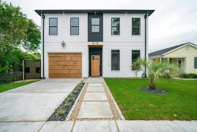 Two-story white house with brown garage door, black accents, and pathway to wooden front door.