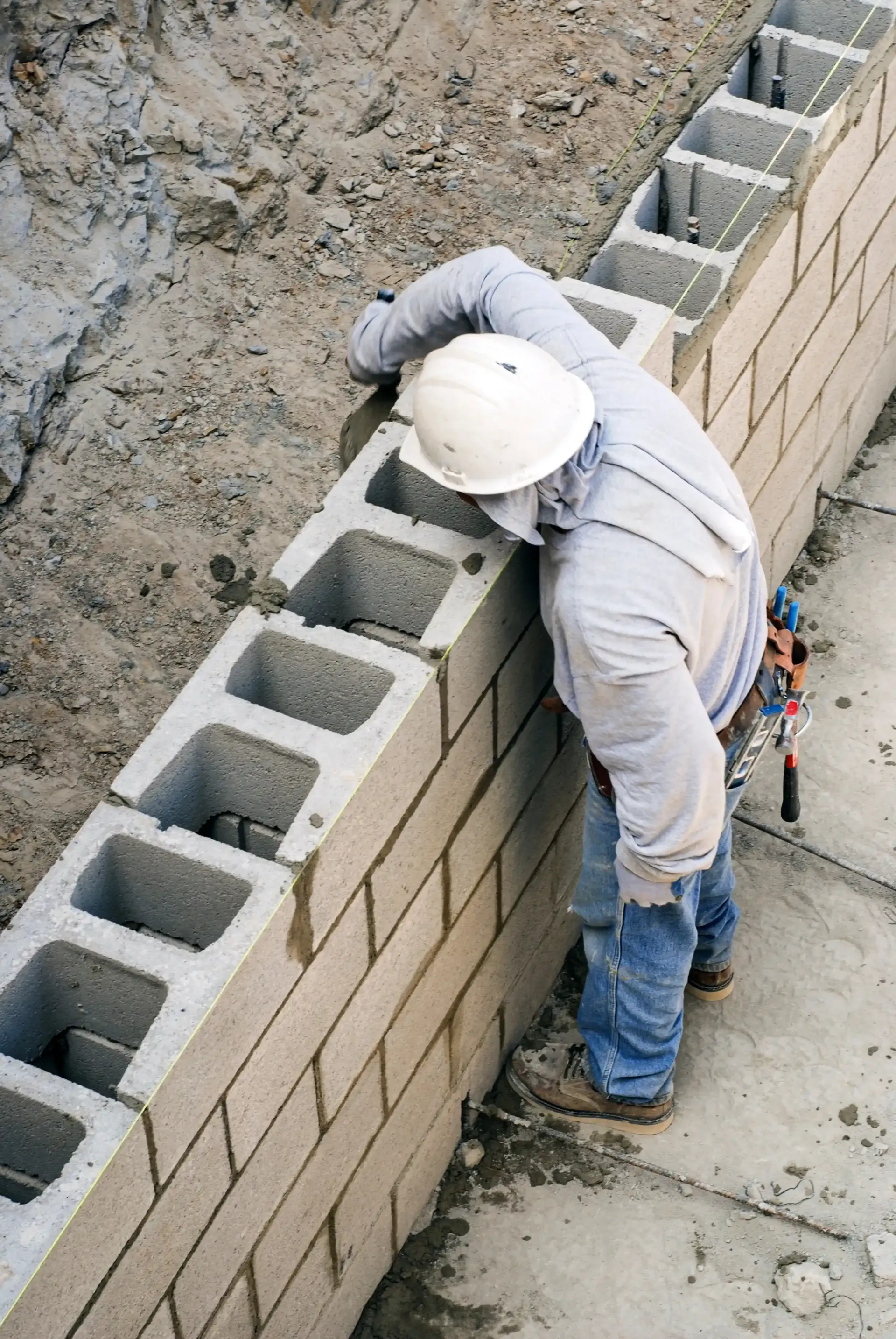 Construction worker wearing a white hard hat building a cinder block wall outdoors.