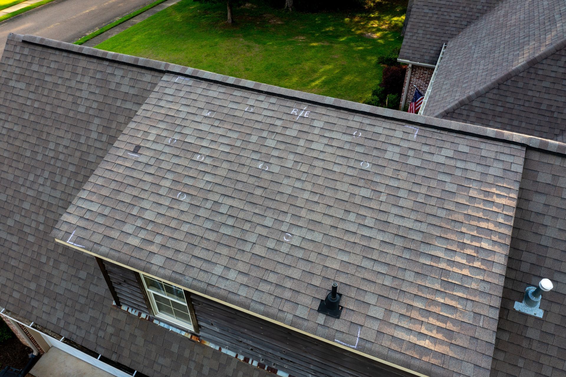 Aerial view of a gray shingle roof with skylights and a green lawn beside it