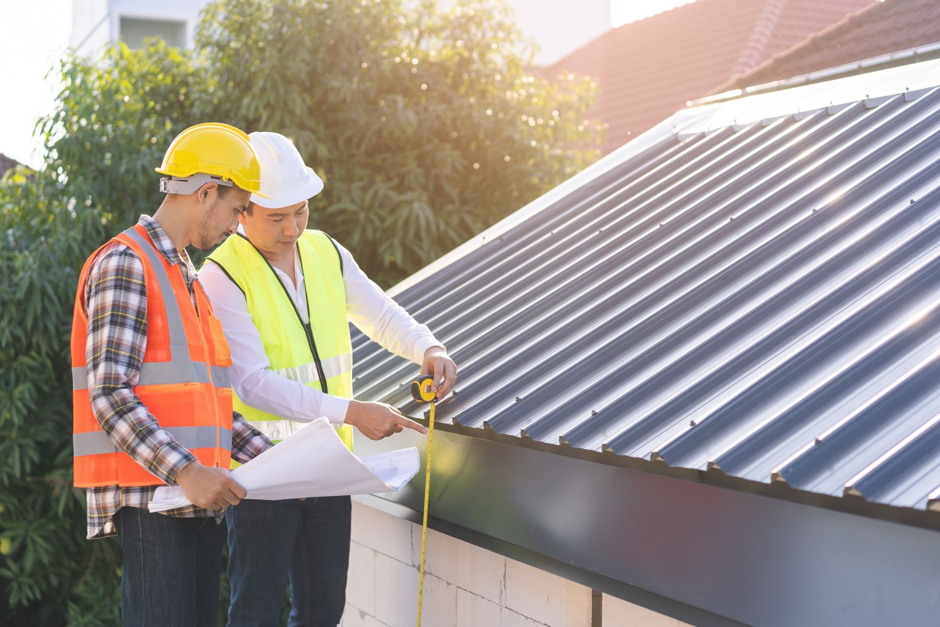 Two workers in hard hats inspect a rooftop with a measuring tape near solar panels.