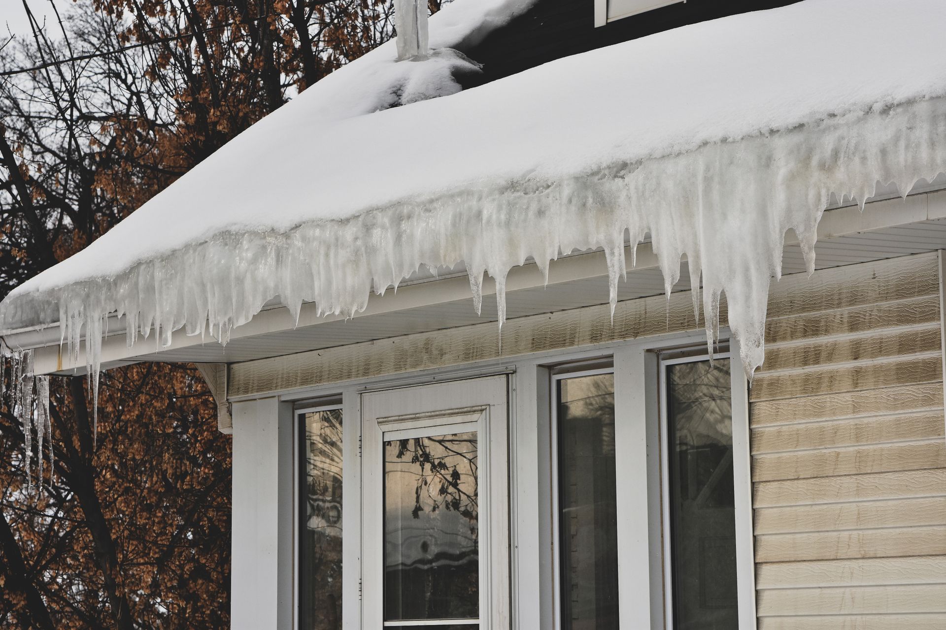 Snow-covered roof with large icicles hanging above windows on a house in winter.