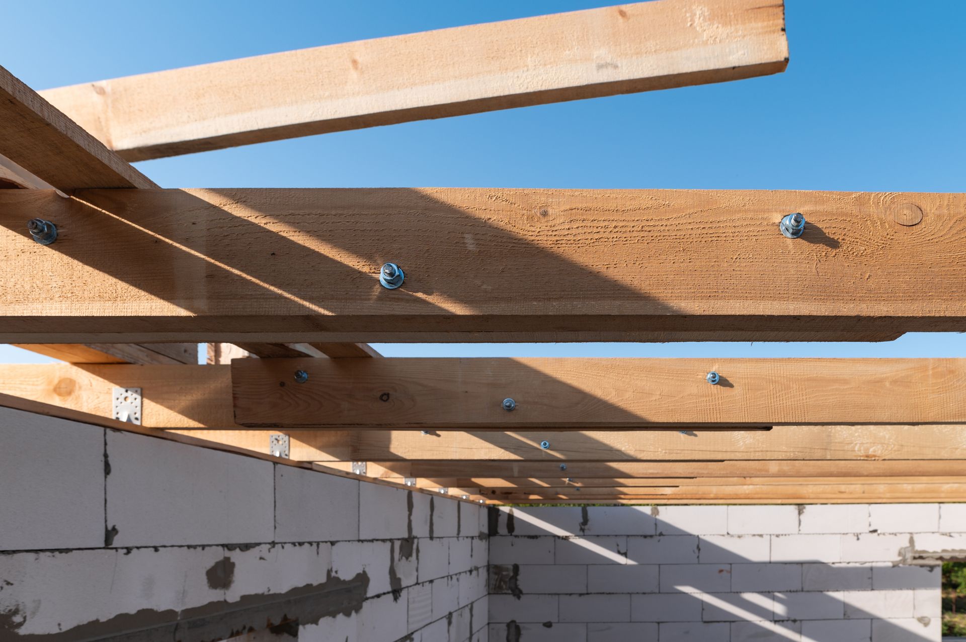 Wooden beams bolted to a brick wall under a blue sky, framing the structure of a building.