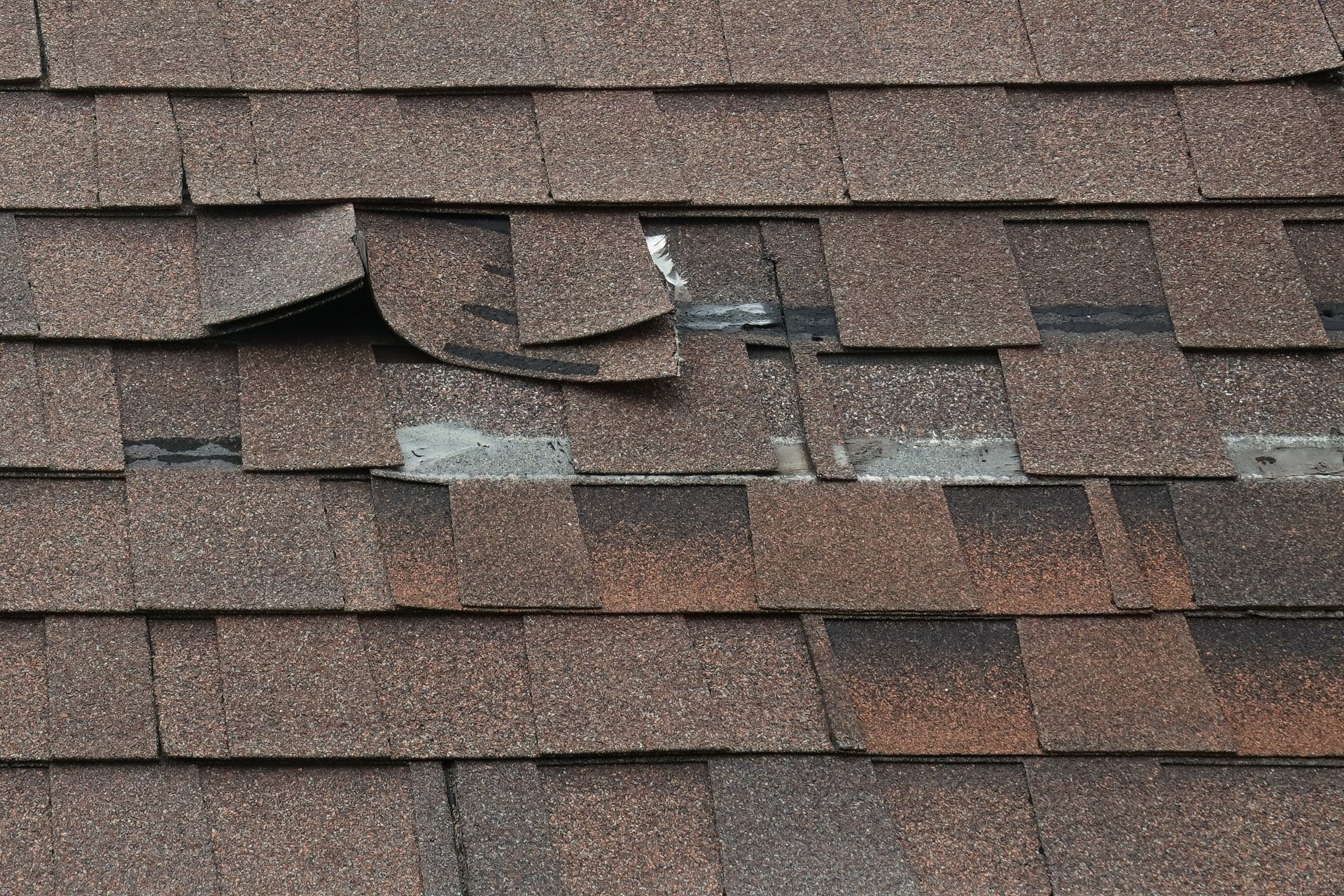 Damaged brown asphalt roof shingles with several loose, torn sections.