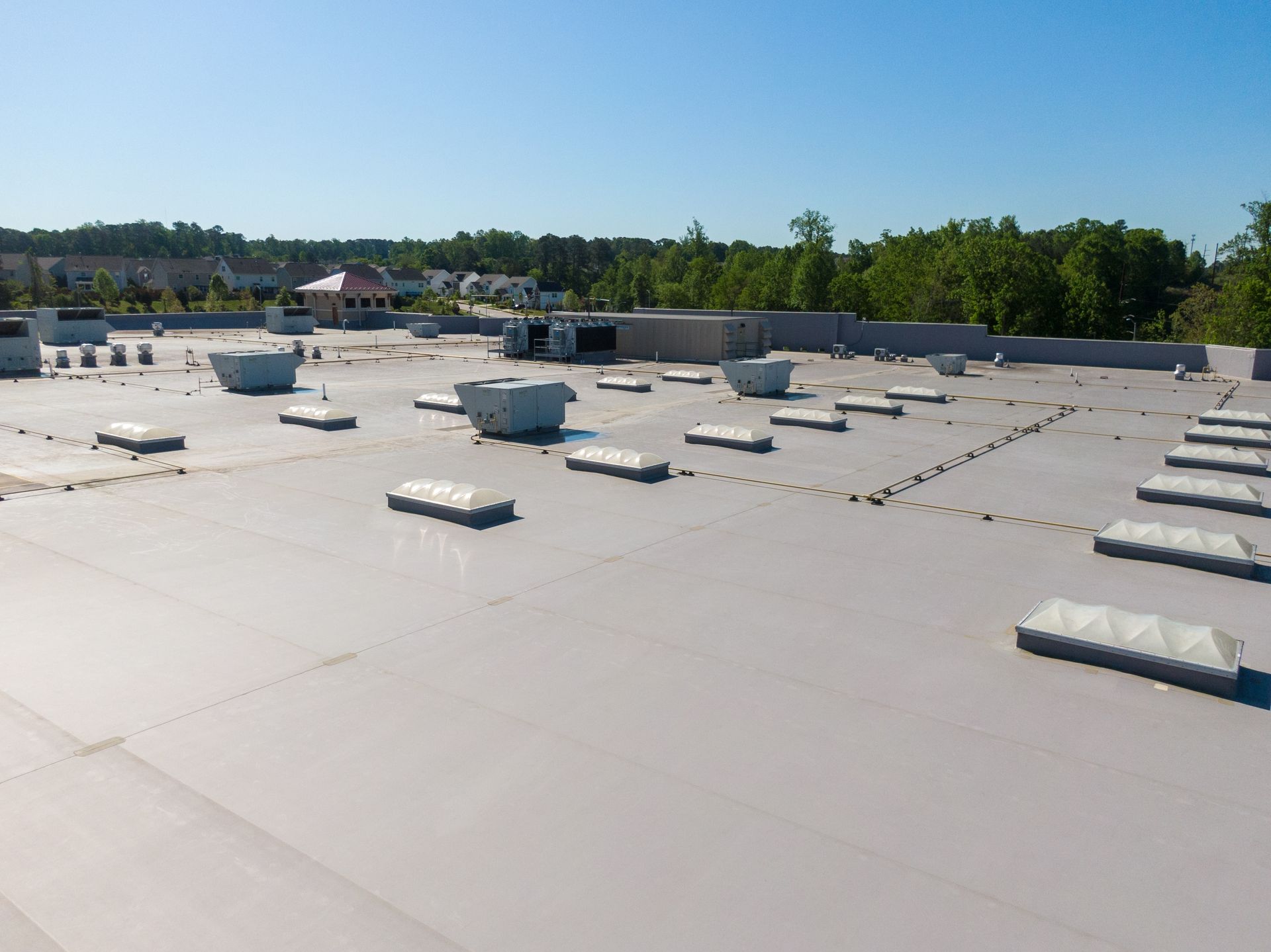 Rooftop with white reflective surface and scattered vents, bordered by trees under a clear blue sky.