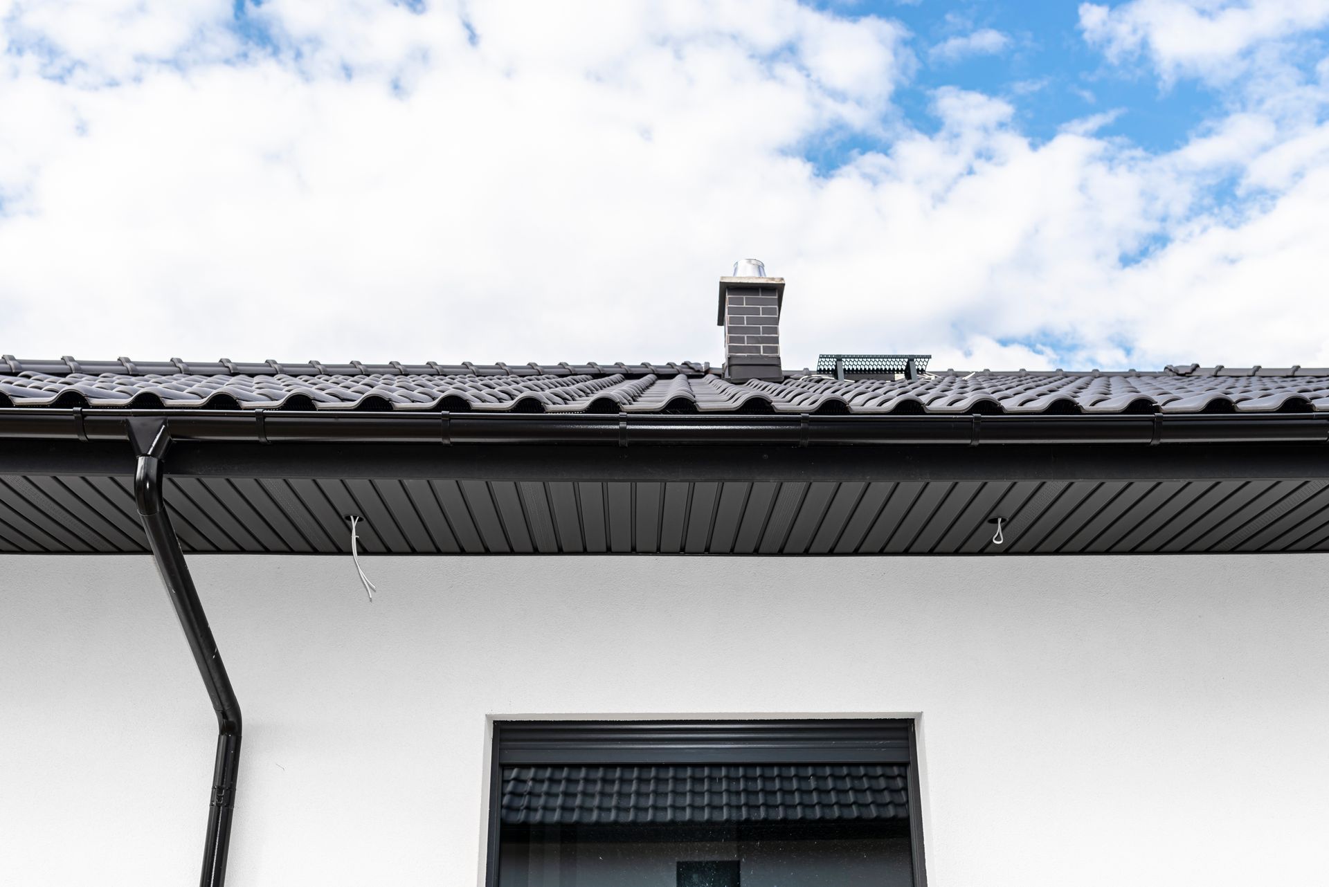 A white house with a black gutter and a chimney on the roof.