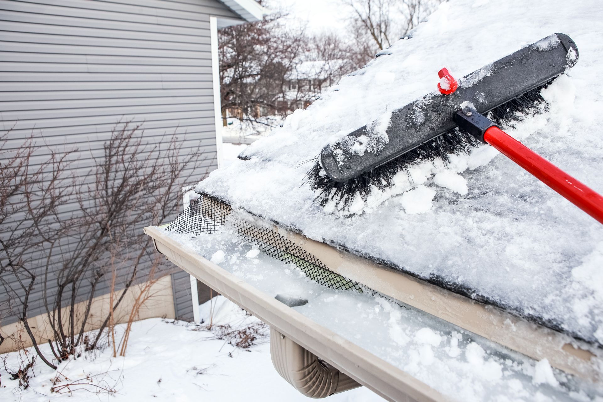 A person is shoveling snow from the roof of a house.