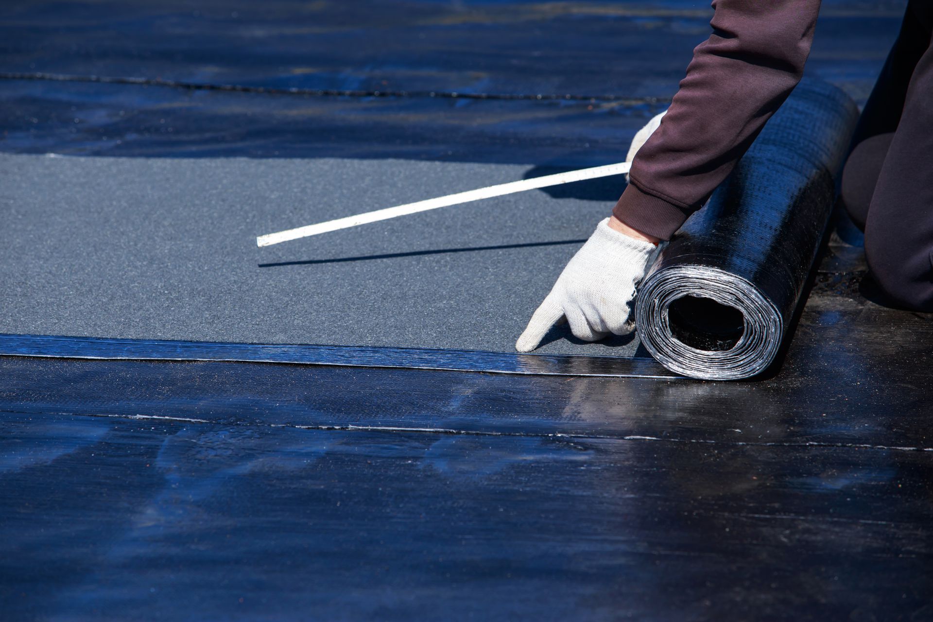 A person is rolling a roll of roofing material on a roof.