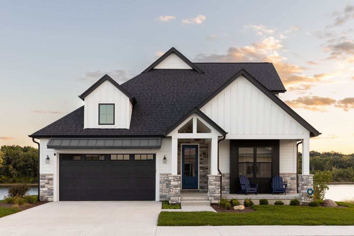 A white house with a black roof and a black garage door.