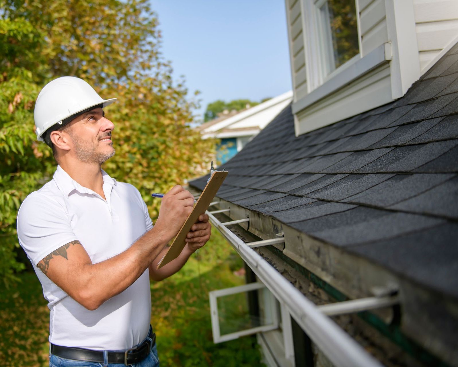 A man is standing on the roof of a house looking at a clipboard.