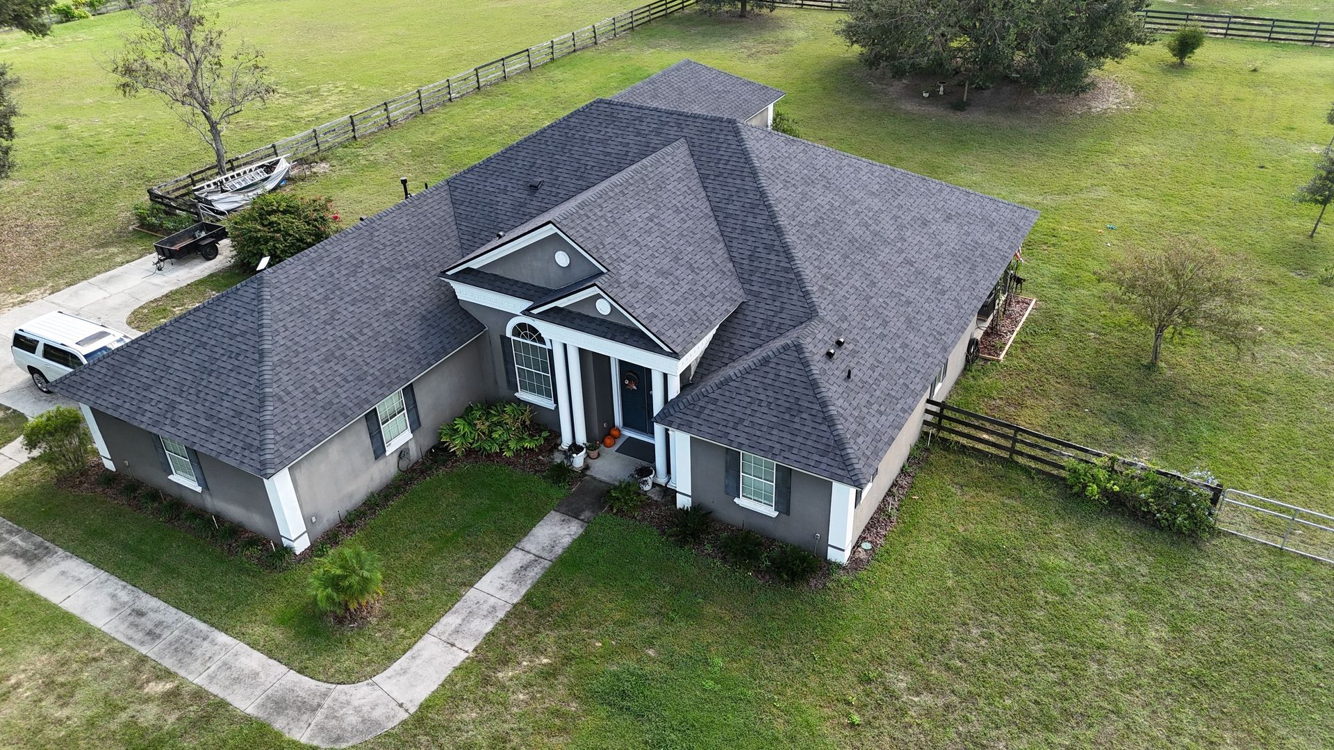 An aerial view of a large house with a gray roof surrounded by grass and trees.