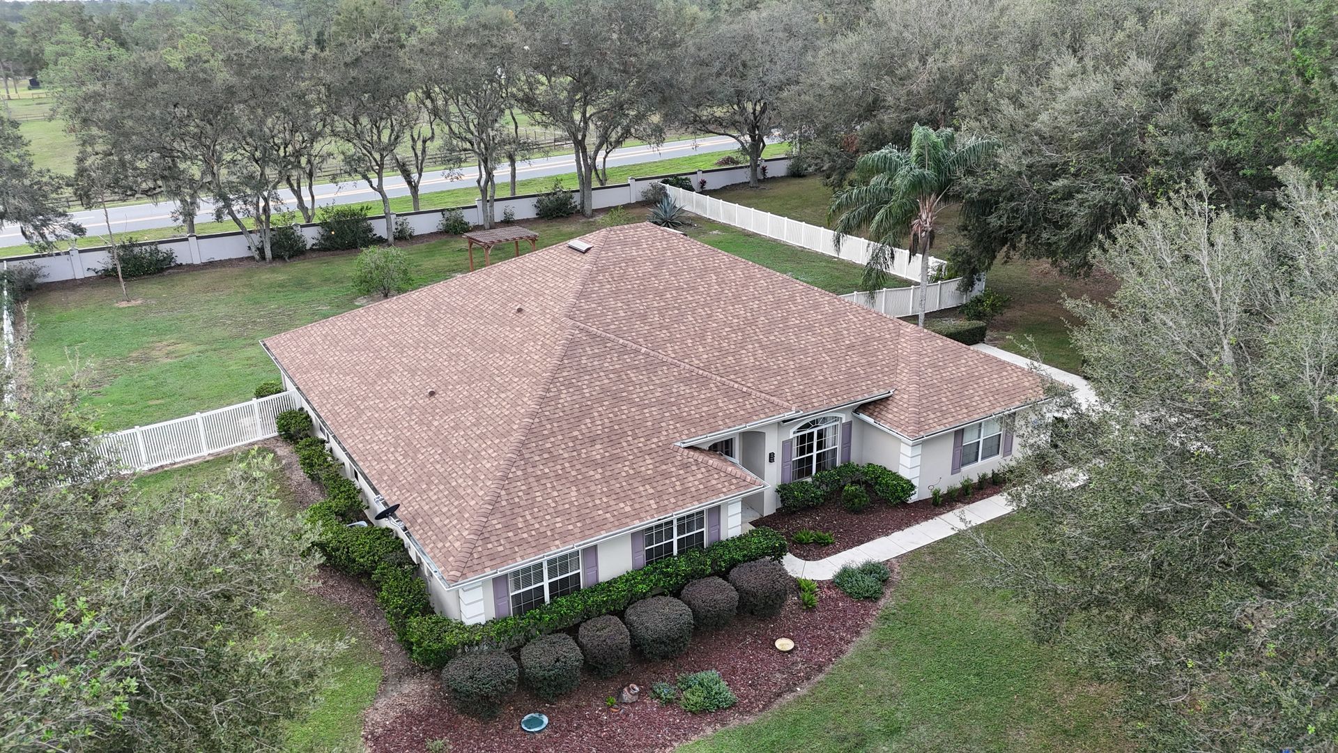 An aerial view of a large white house with a brown roof surrounded by trees.