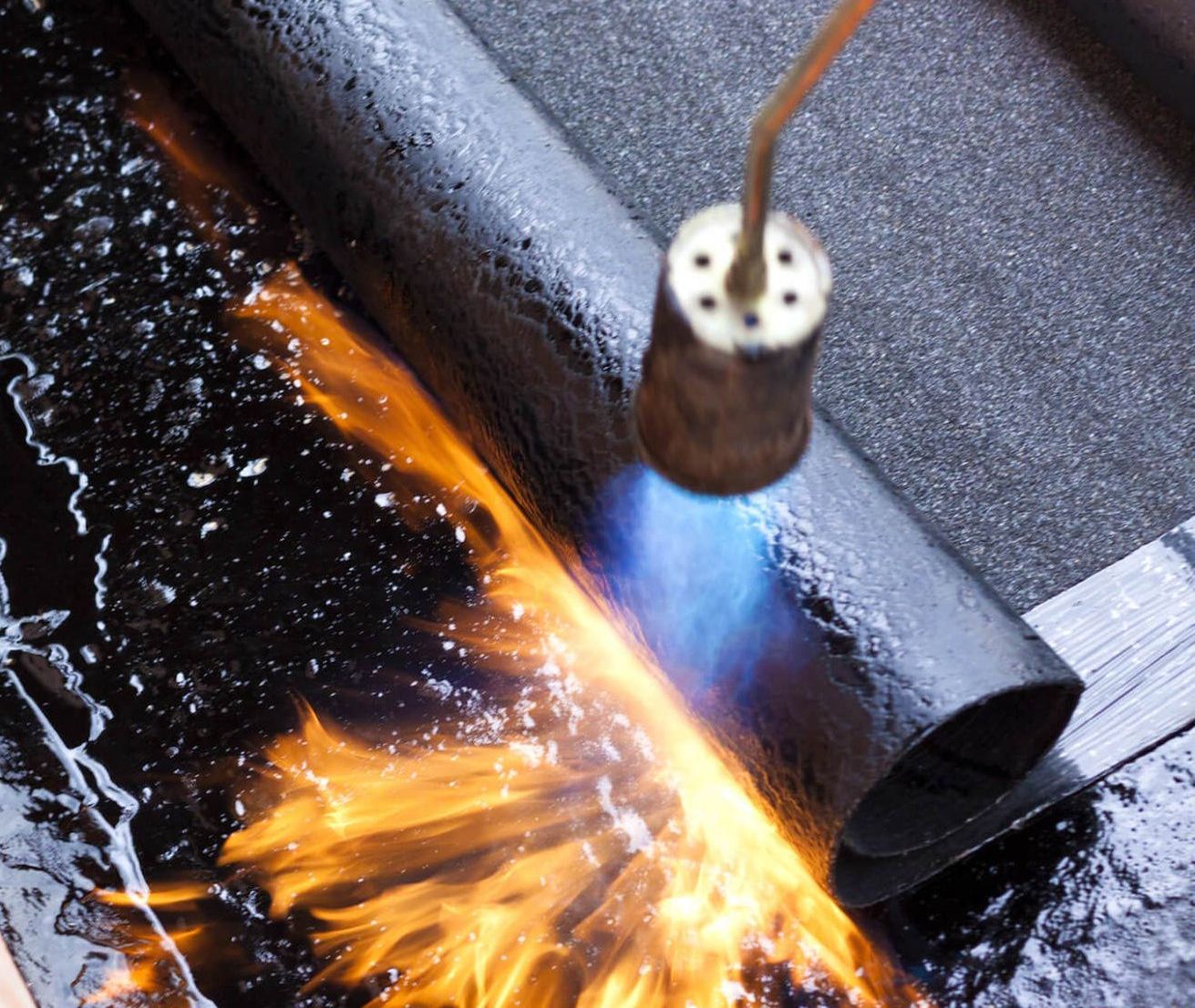 Un ouvrier utilise une torche pour faire fondre des matériaux de toiture, créant ainsi un effet semblable à celui du feu.