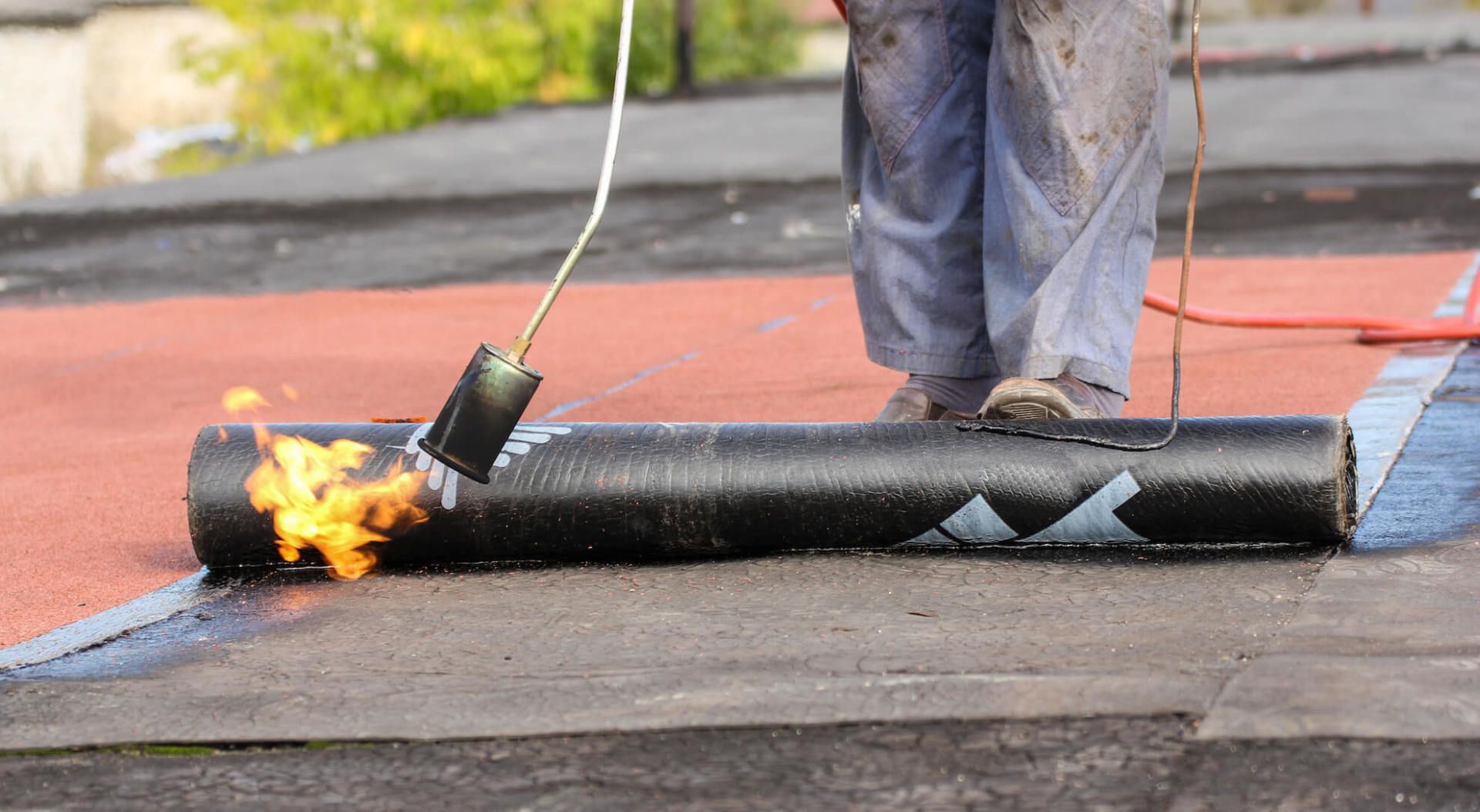 Personne utilisant un chalumeau pour appliquer un rouleau de matériau de toiture sur un toit plat.