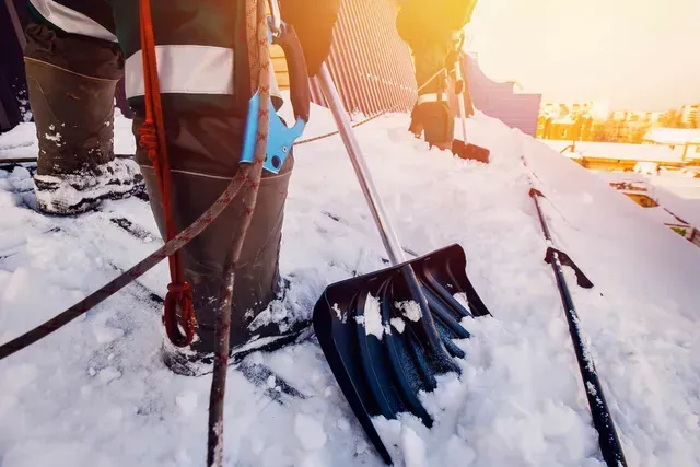 Une personne enlève la neige d'un toit avec une pelle.
