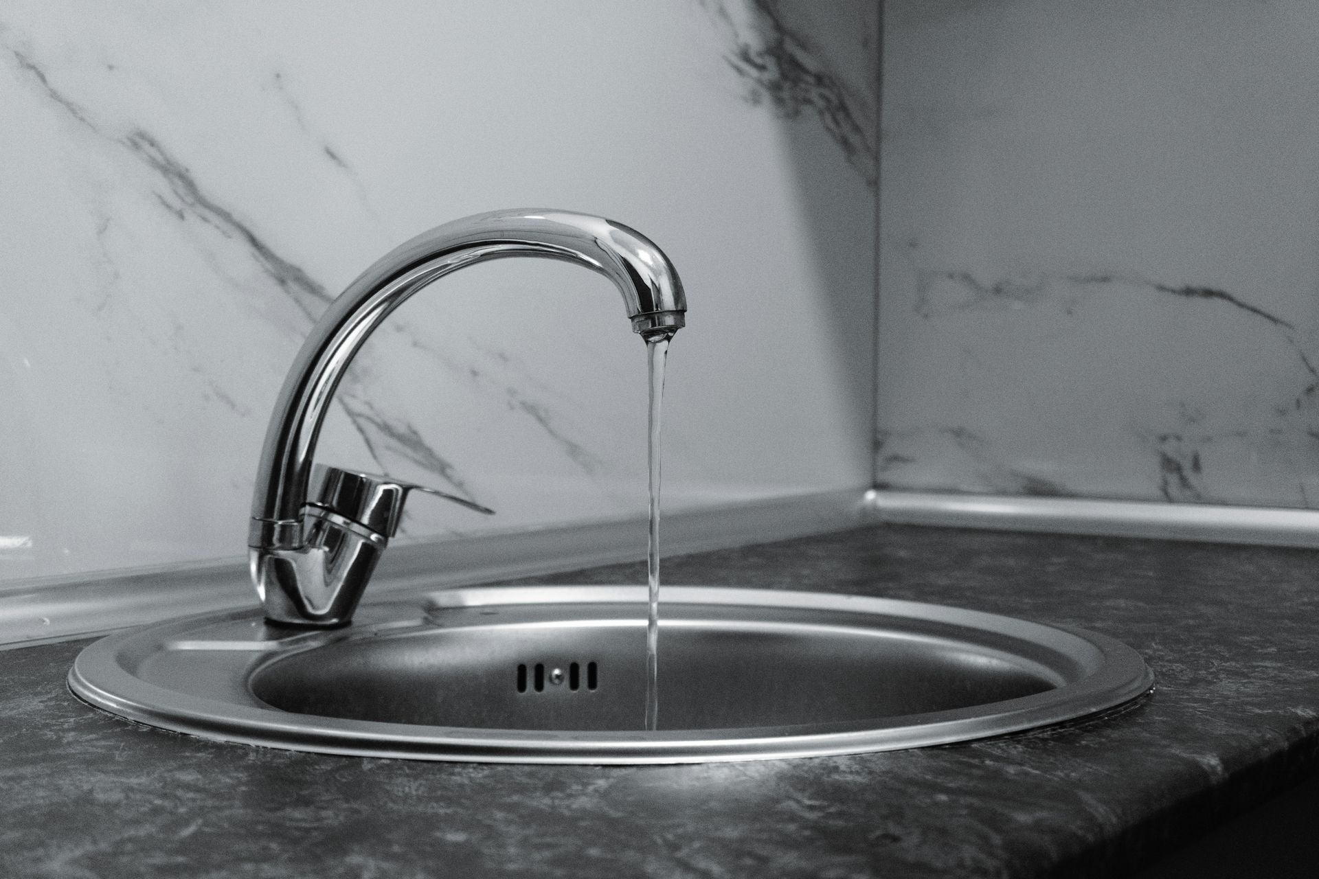 Under-sink view: stainless steel sinks, plumbing, waste bin, and cabinet door.