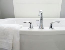 A white bathtub with chrome fixtures, a white towel, and a gray wall in the background.
