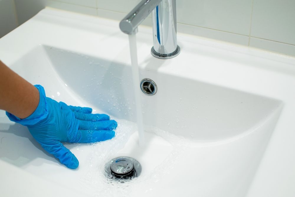 Under-sink view: stainless steel sinks, plumbing, waste bin, and cabinet door.