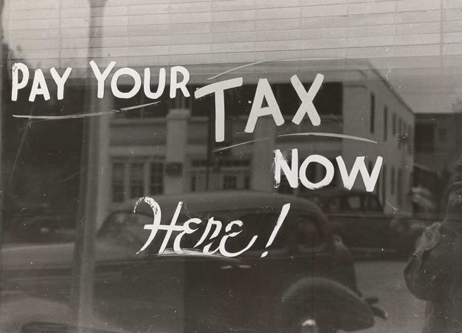 A black and white photo of a window with a sign that says pay your tax.