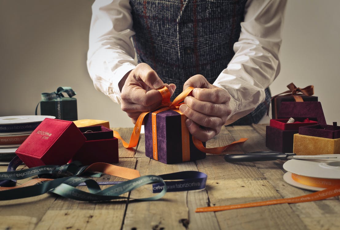 a man is tying a ribbon around a gift box on a wooden table .
