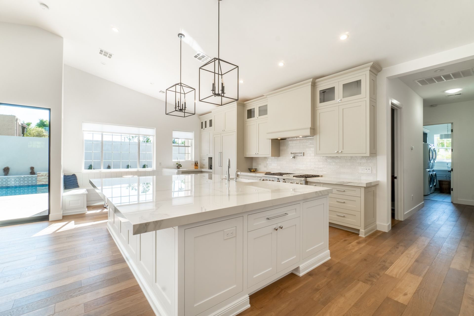 Bright modern white kitchen with large island, pendant lights, wood floors, and open dining area