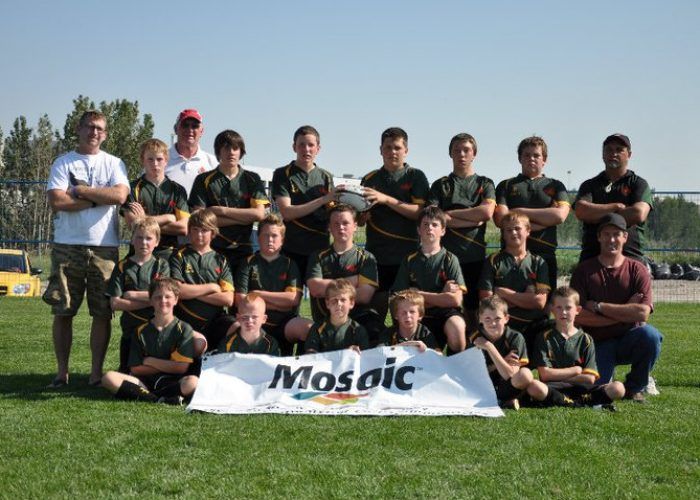 A sports team in green jerseys poses outdoors on a grassy field behind a 