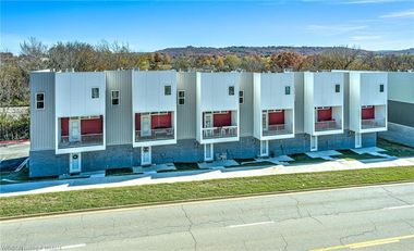 Row of modern townhouses with grey and white siding, red balconies, and blue sky.